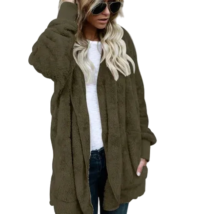 Person wearing an olive green cardigan over a white top and dark jeans against a gray concrete wall.